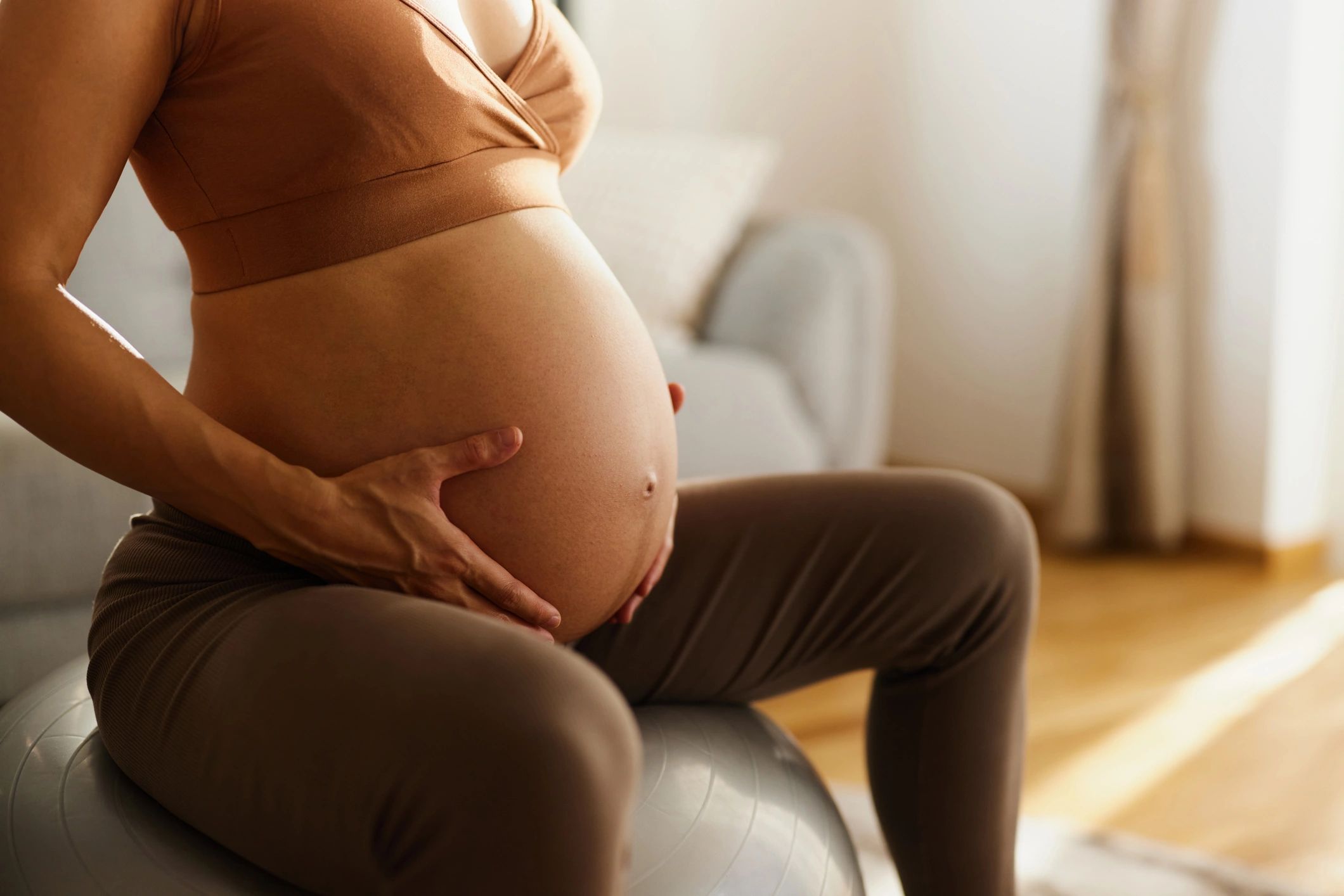 Pregnant woman holding her belly while sitting on an exercise ball.