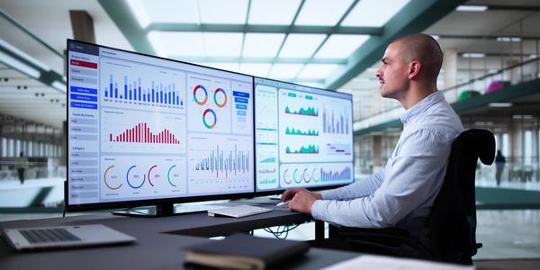 Man analyzing data on dual monitors in a modern office.