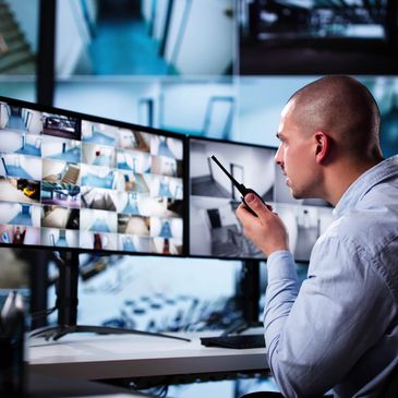 Security guard monitoring multiple surveillance screens with a walkie-talkie.