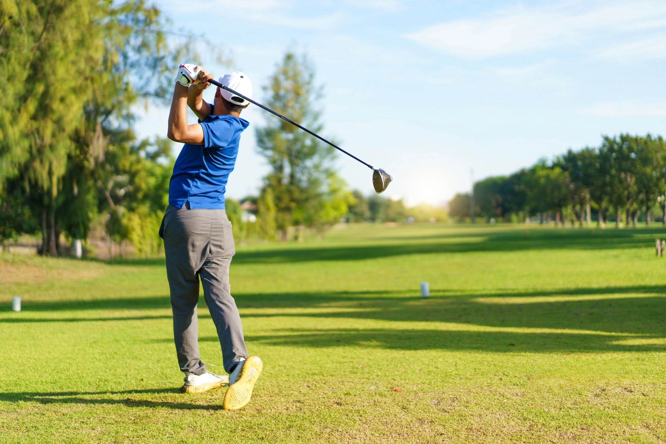Golfer swinging a club on a sunny golf course.