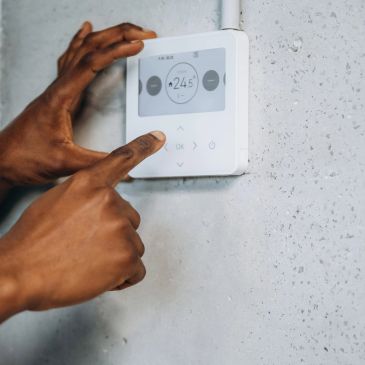 Person adjusting a thermostat on a wall.