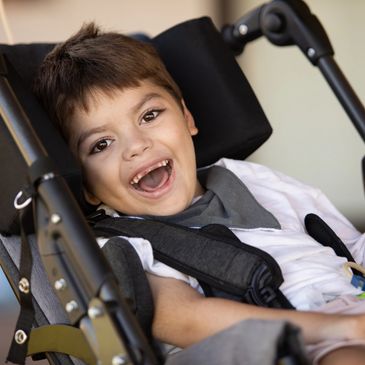 Smiling child in a supportive wheelchair harness.