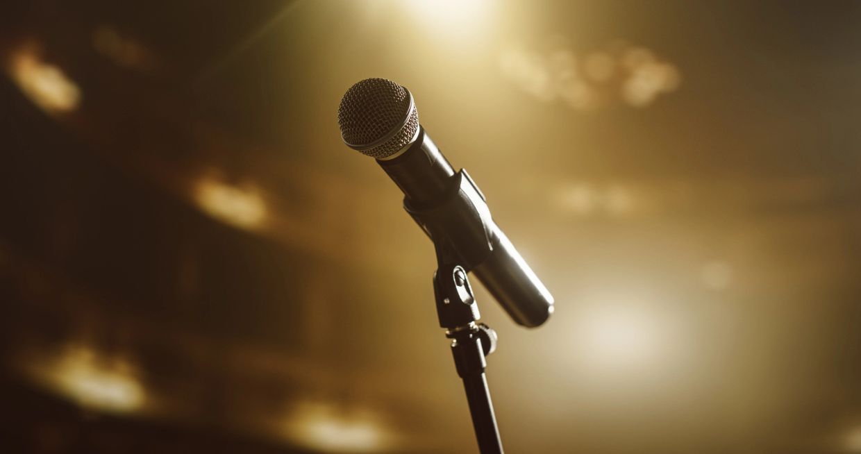 A microphone on a stand illuminated by warm stage lighting.