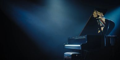 A grand piano illuminated by a single spotlight on a dark stage.