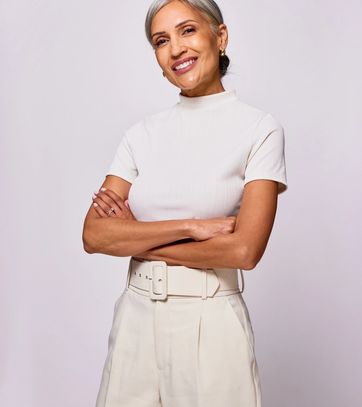 Smiling woman in beige outfit with folded arms.