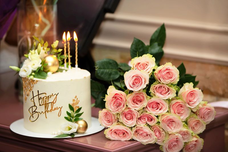 Cake with the inscription Happy Birthday and a bouquet of pink roses on the table. Preparation for the anniversary.