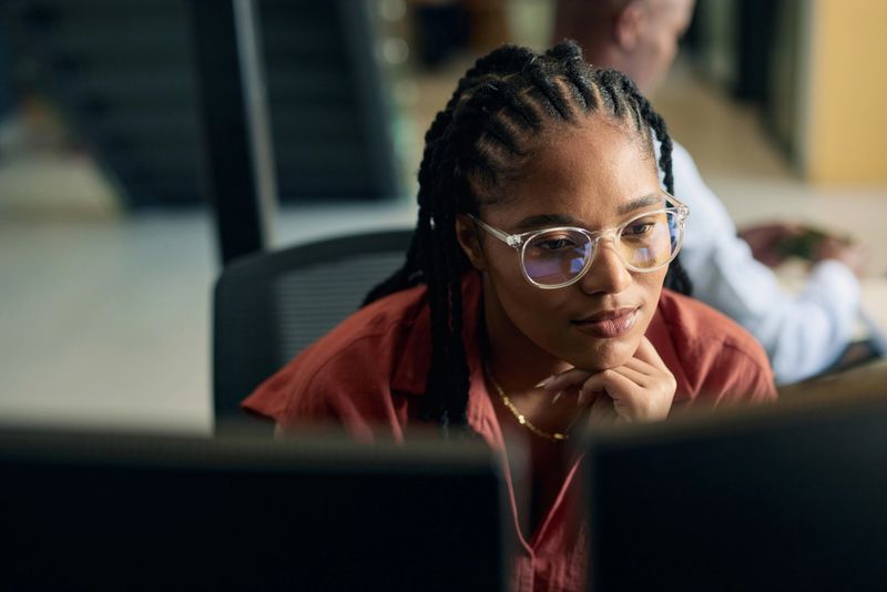 Young woman programmer focused on her work, coding on dual monitors in a modern office environment