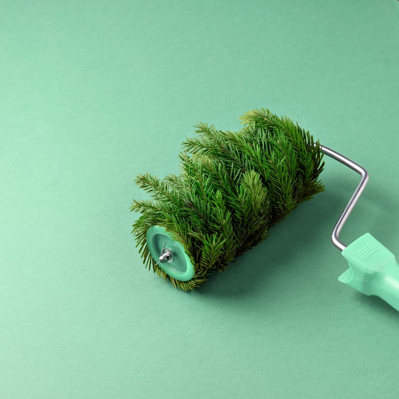 Paint roller covered with fir branches on a green background. A creative and unconventional concept combining nature and creativity, creating a fresh festive atmosphere.