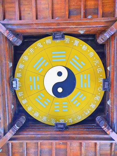 Yin-yang symbol with I Ching trigrams on a yellow circular board in wooden ceiling.