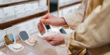 Person testing makeup with a compact mirror in a store.