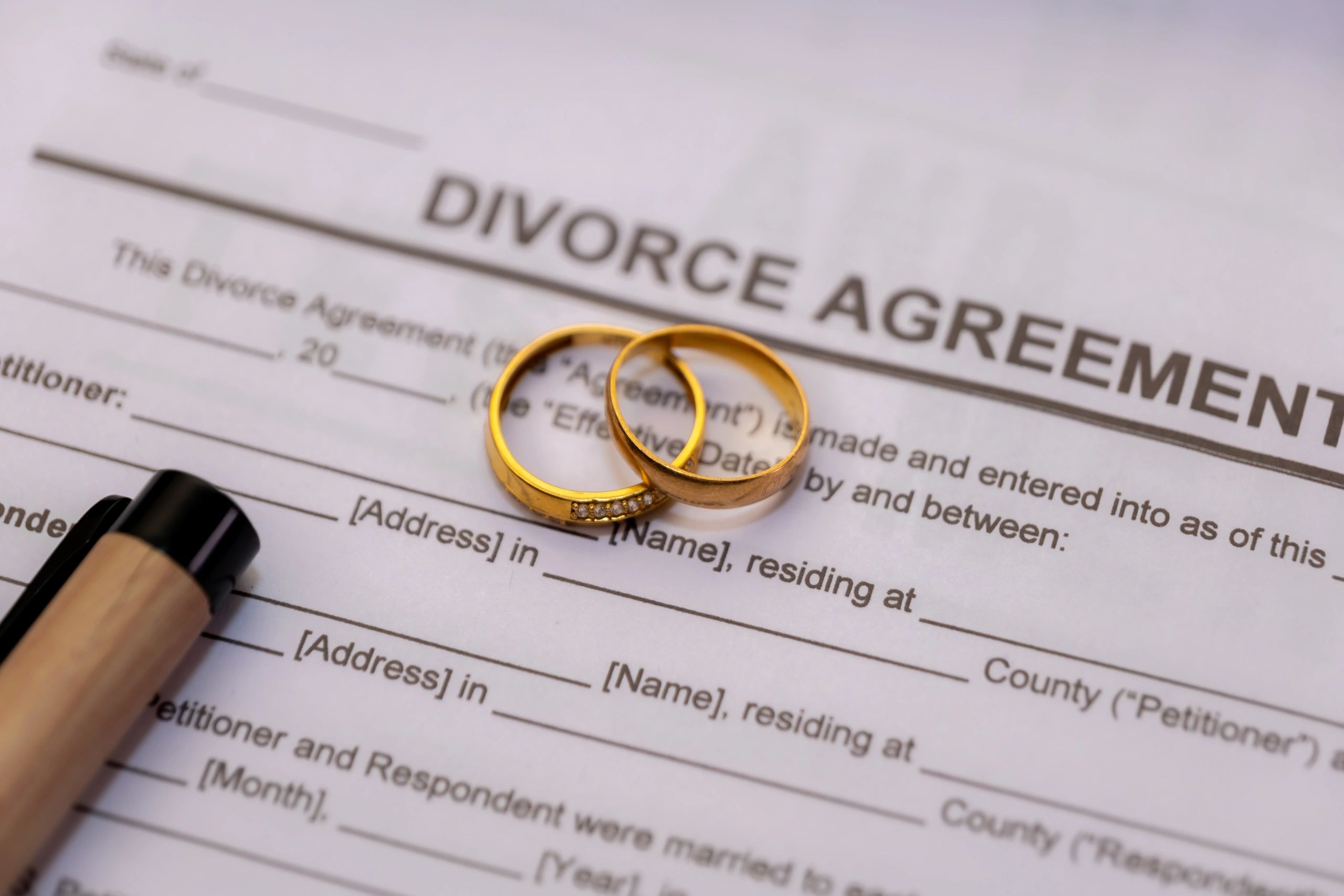Two gold wedding rings on a divorce agreement form with a pen nearby.