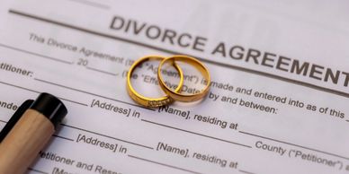 Two gold wedding rings on a divorce agreement form with a pen nearby.