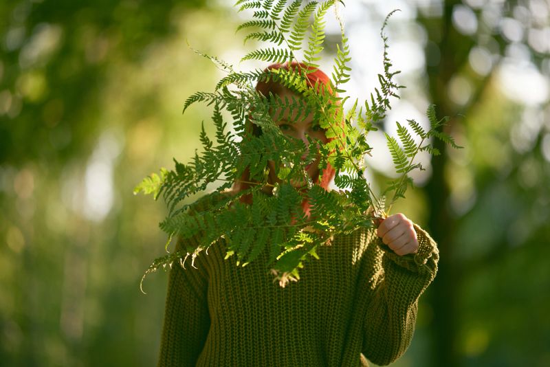 A serene red-haired woman framed by ferns and golden light, embodying the calm beauty of nature.