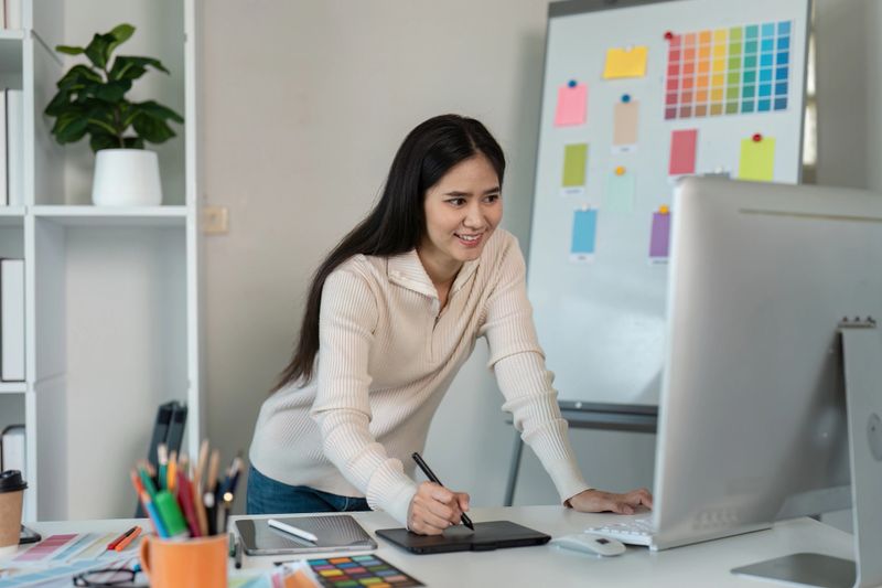 A graphic designer uses a digital tablet in a modern office, surrounded by colorful design elements and tools.
