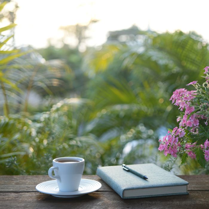 A cup of coffee and a notebook with a pen on a wooden table outside.