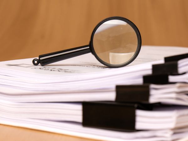 Magnifying glass on top of neatly stacked documents with black binder clips.