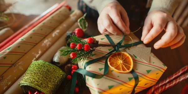 Hands wrapping a festive gift with green ribbon and dried orange.