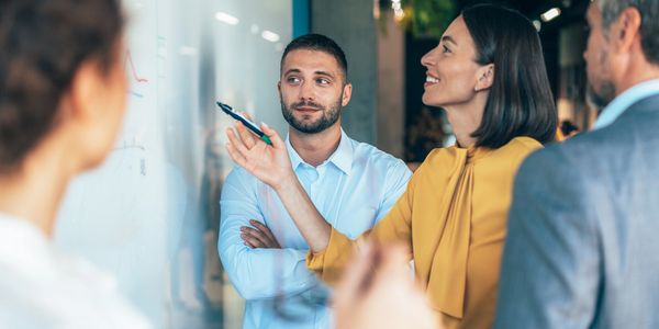 Colleagues discussing ideas at a whiteboard in an office meeting.