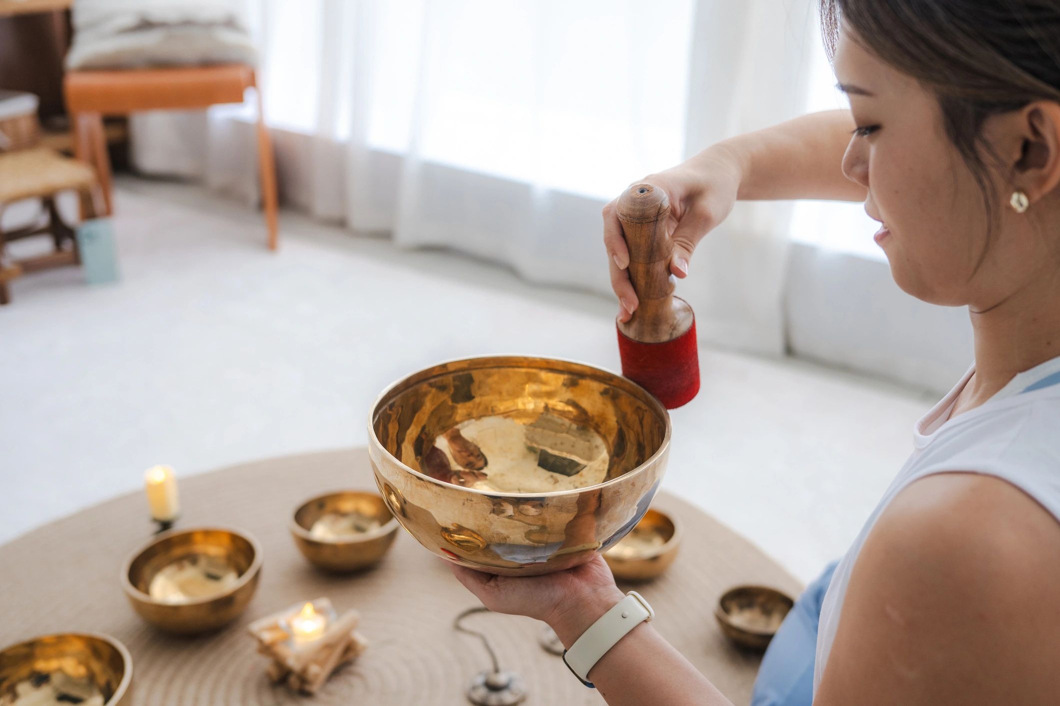 Woman using a wooden mallet with a singing bowl.
