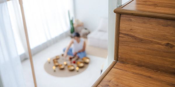 Wooden staircase with a blurred person meditating below surrounded by candles and bowls.