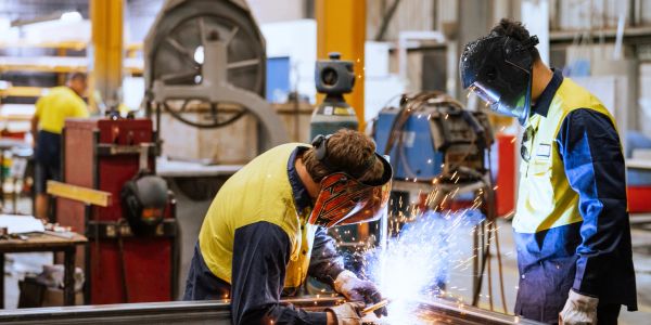 Soudeur travaillant dans un atelier avec un collègue observant.