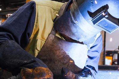 A welder working on metal in an industrial workshop with sparks flying.