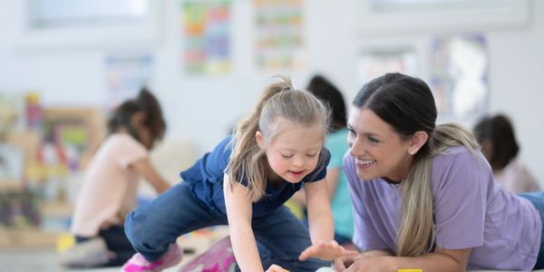 A young girl and a woman playing with colorful balls and rings on the floor.