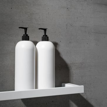 Two white pump bottles on a white shelf against a gray concrete wall.
