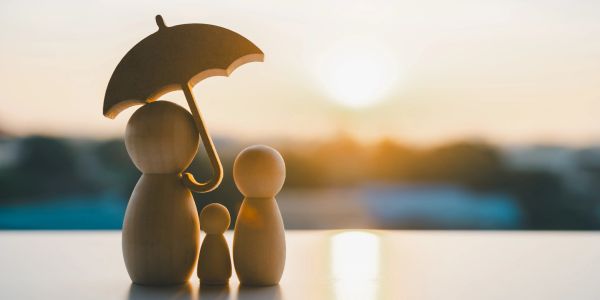 Wooden figures under one umbrella at sunset.