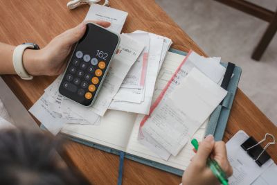 Person calculating expenses with a calculator and receipts on a notebook.