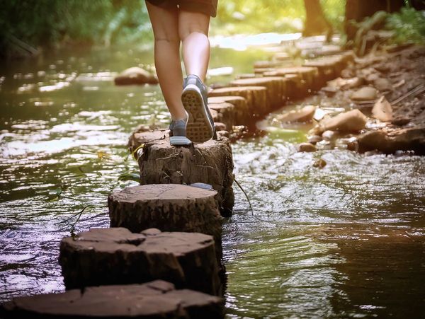 Person walking on wooden stepping stones across a shallow stream.