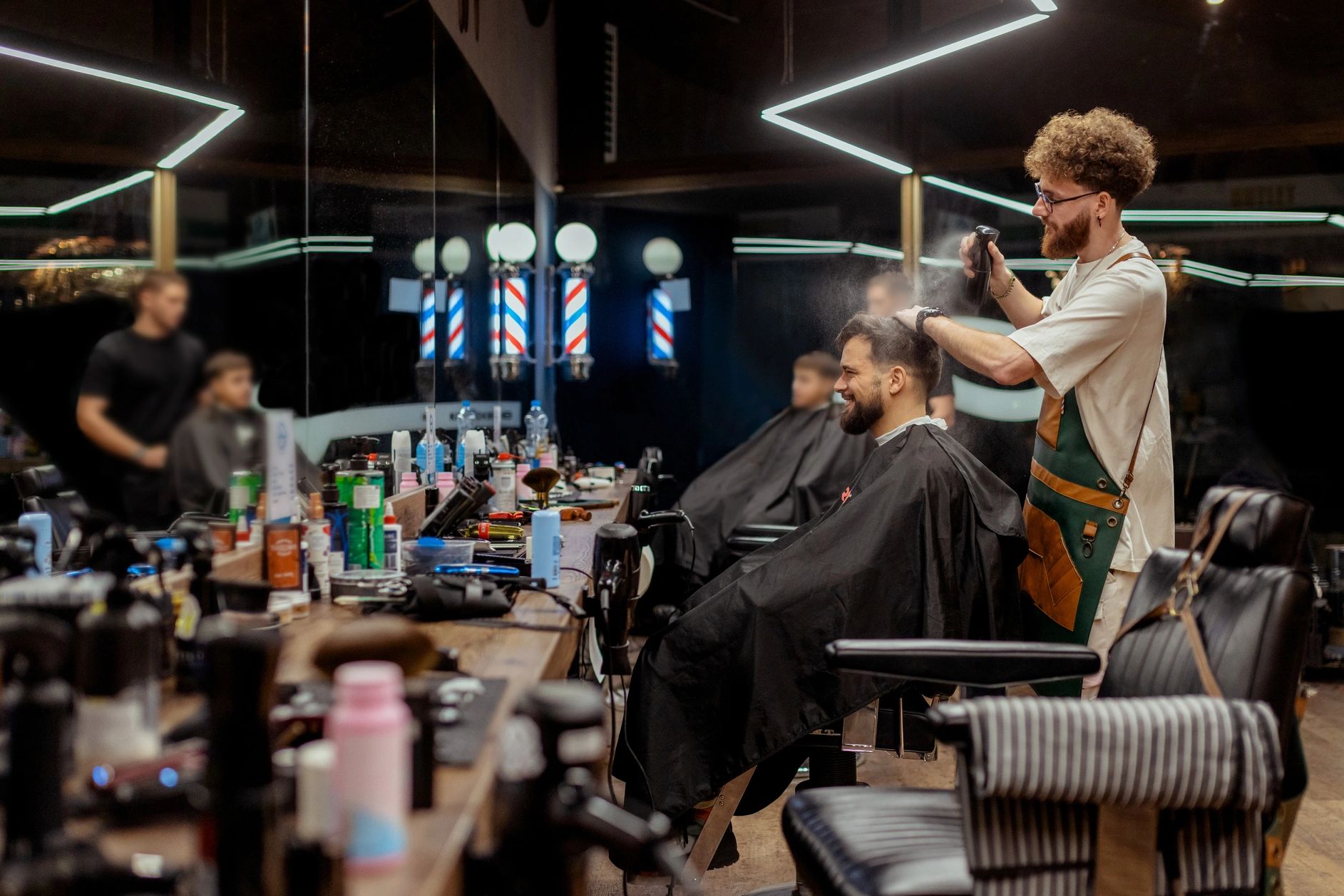 Barber spraying hair of a smiling client in a modern barbershop.
