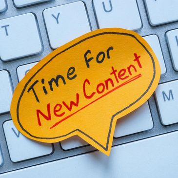 Sticky note on keyboard reads 'Time For New Content' urging fresh ideas.