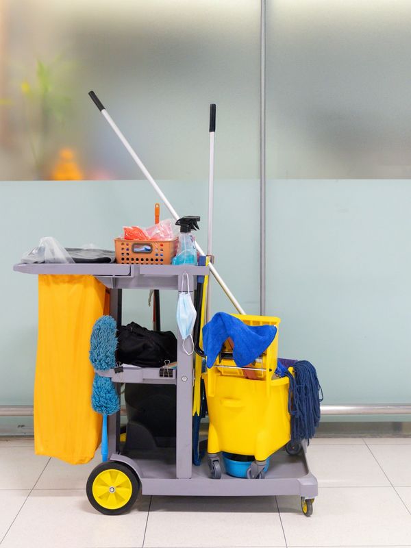 A janitorial cart with cleaning supplies and a yellow mop bucket.
