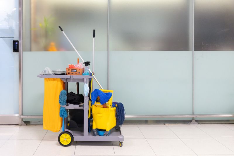 A cleaning cart with a yellow bucket and a blue mop. The cart is full of cleaning supplies