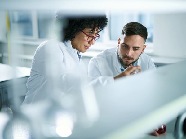 Two scientists in lab coats collaborating on an experiment in a modern laboratory.