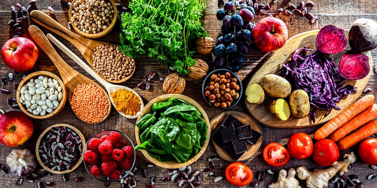 Colorful assortment of fresh fruits, vegetables, nuts, and spices on a wooden table.