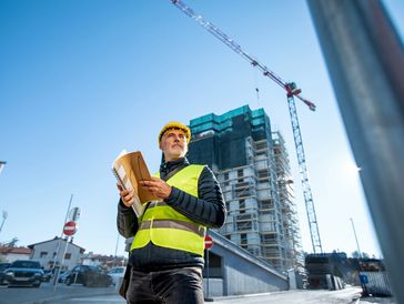 Construction worker in safety gear inspecting plans at a building site.