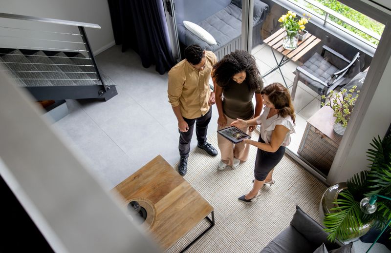 High angle view of a couple discussing details of a house with their real estate agent while looking at a brochure using a digital tablet