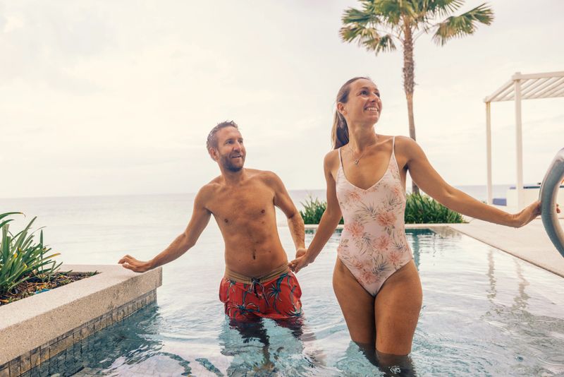 Man and woman in swimsuits relaxing together in a luxurious infinity pool. The serene ocean view creates a romantic and tranquil atmosphere, perfect for a tropical getaway.