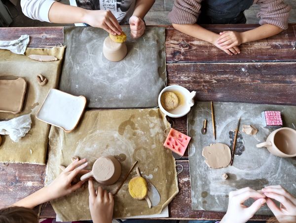 People shaping and smoothing clay on mats at a pottery workshop.