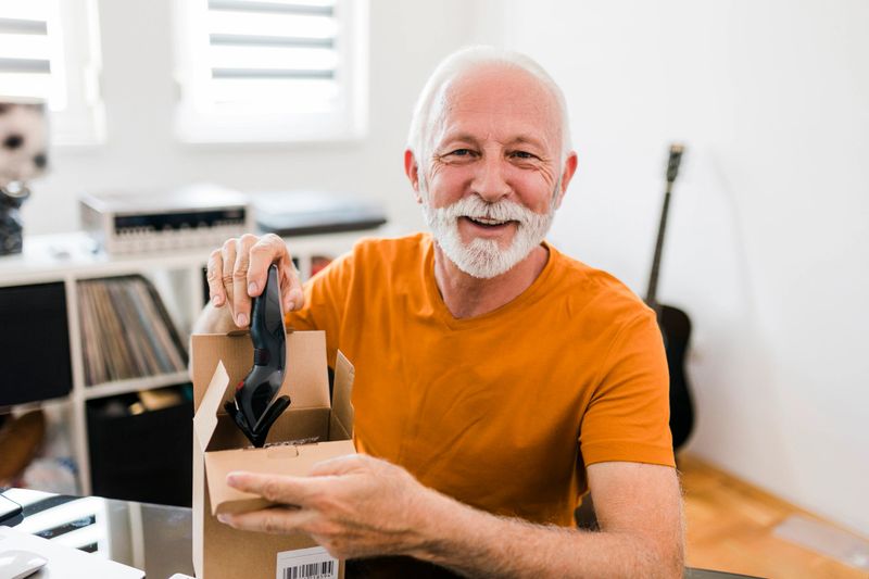 Smiling senior Male social media technology influencer recording unboxing video at home
