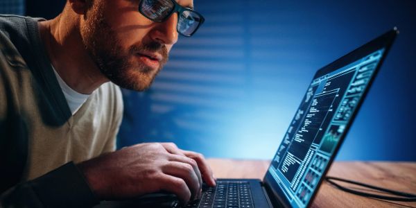 Man intensely working on laptop with coding on screen.
