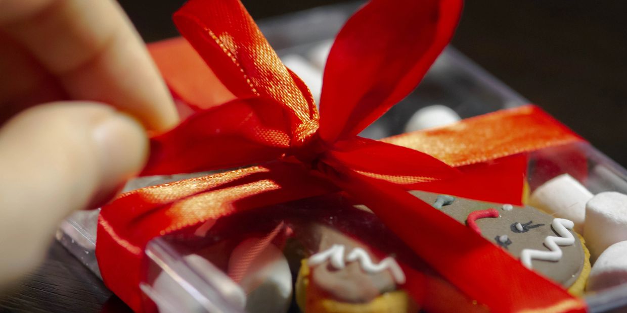 A person is opening a gourmet cookie gift that is wrapped with a red bow.