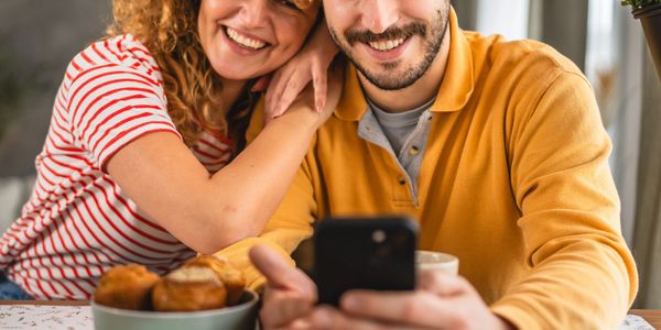 Couple smiling while looking at a smartphone during breakfast.