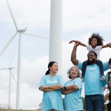Happy volunteers in blue shirts near wind turbines.