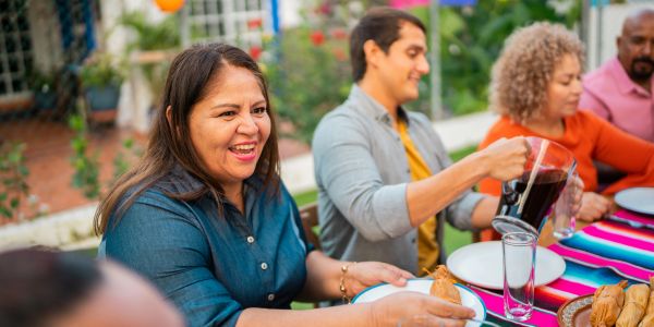 A woman serves food and a man pours a drink at a dinner table.