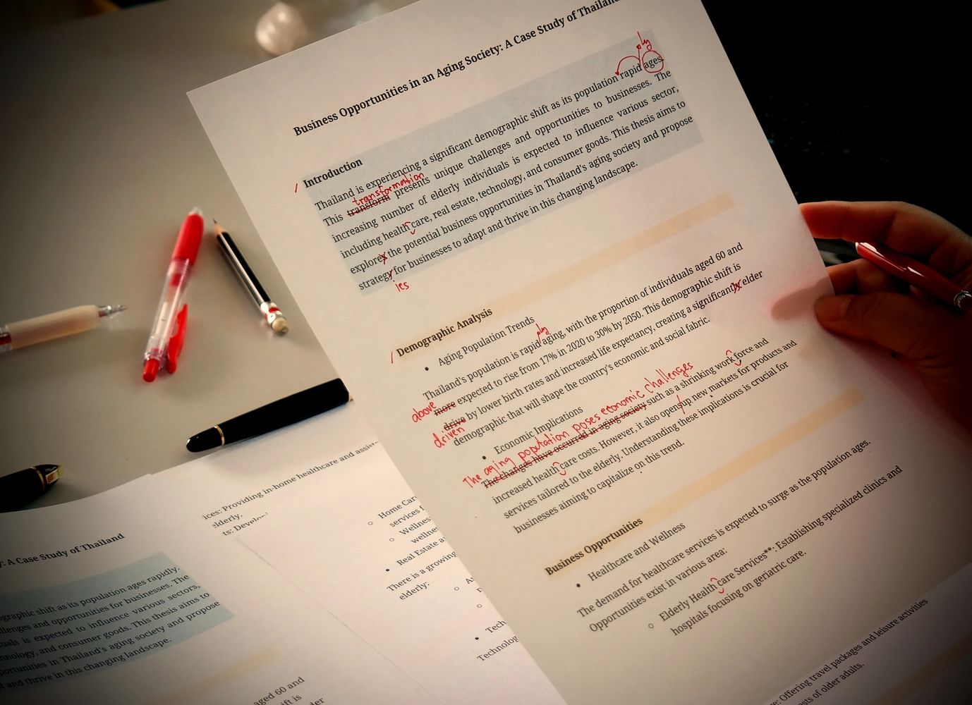 Black pencils in a gray holder next to a stack of white magazines with a camera in the background.