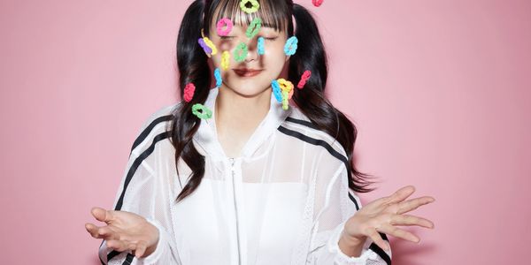 Young woman tossing colorful hair ties in front of a pink background.