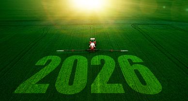 A tractor sprays a green field with '2026' written on it under a bright sun.